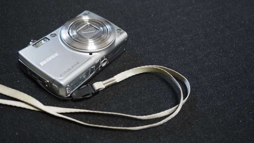 FujiFilm FinePix F100fd の写真。カメラ本体はやや小さく映し出されているがストラップも映している。
